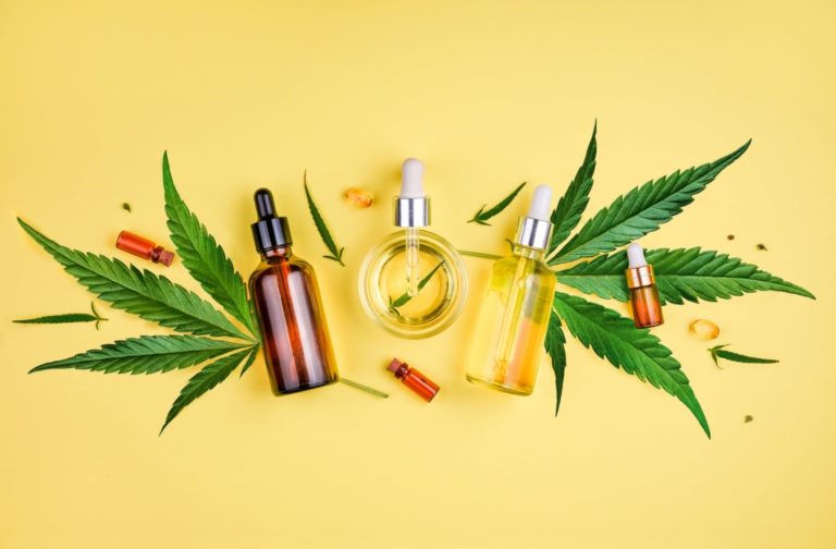 Assorted CBD oil bottles and capsules arranged with hemp leaves on a yellow background, representing cannabidiol products and natural wellness.